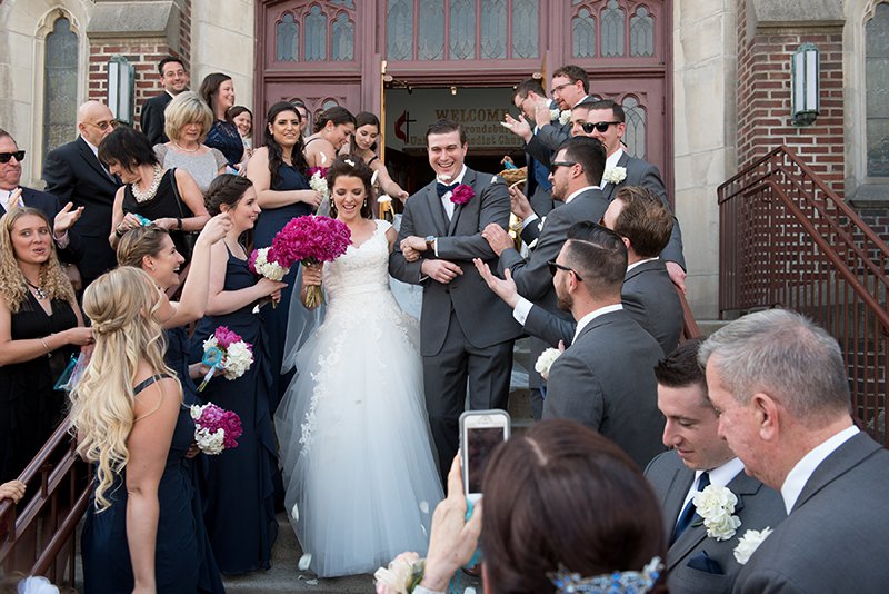 Crowd shot of bride and groom processing out the front steps of a church, surrounded by friends and family