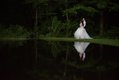 Dramatic nighttime shot of bride and groom strolling near a pond, reflected in the still water