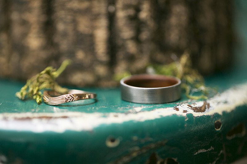 Depth of field photo of custom wedding bands on distressed table with greenery