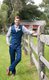 Groom in blue vest and floral bowtie leaning on split-rail fence