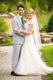 Bride and groom in white lace dress and grey summer linen suit posing outside on stone walkway