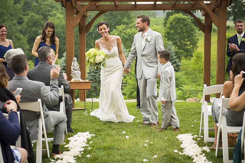 Bride, groom and child recessing at outdoor wedding ceremony with pergola