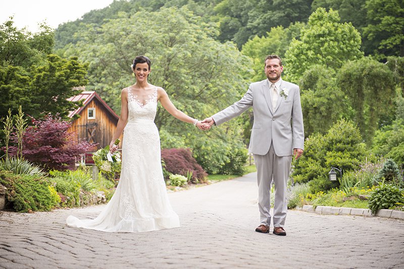 Bride and groom posing outdoors, standing hand-in-hand, white lace dress and light grey summerweight suit